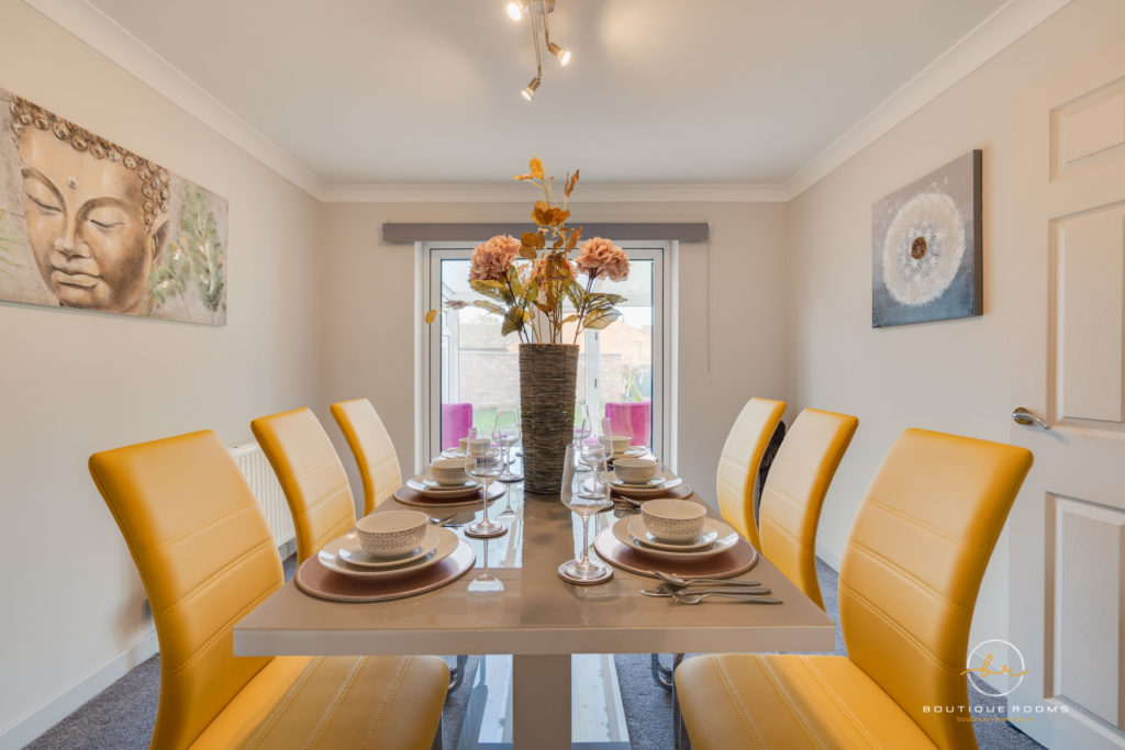 Close up of glass dining table with yellow leather chairs. On top of the table there is a vase of sunflowers.