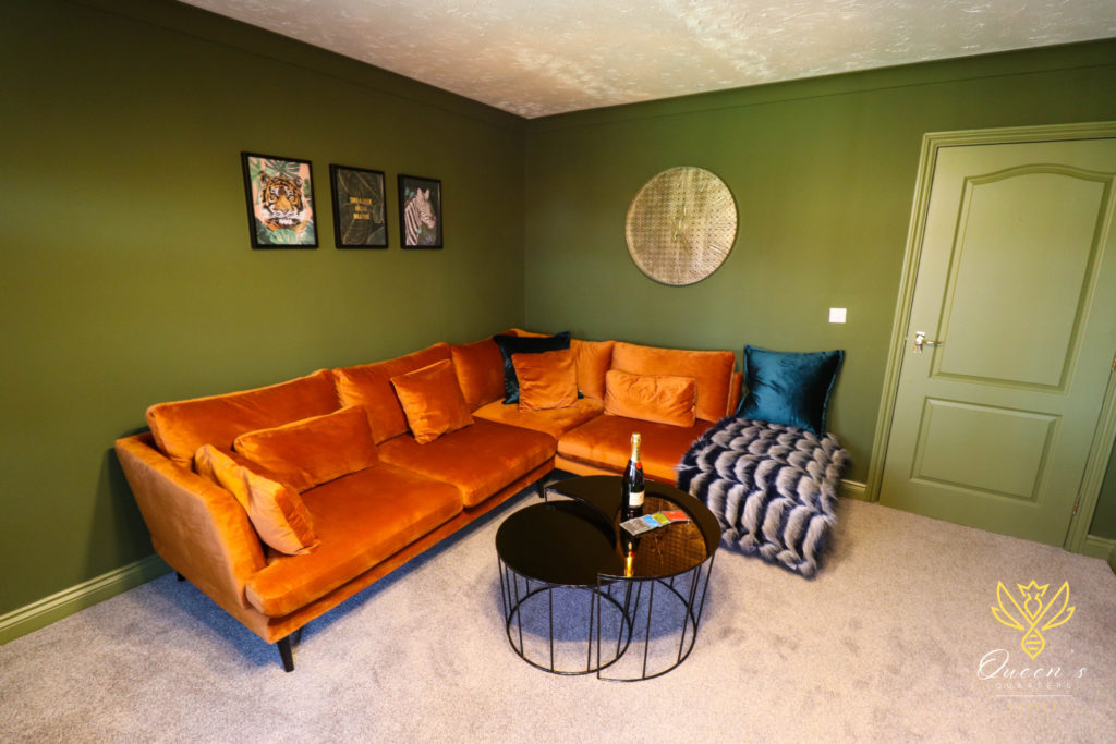 Set in the green living room of our accommodation in Huntingdon, an orange velvet corner sofa opens to the living room. A bottle of Prosecco sits on a black coffee table in the centre.